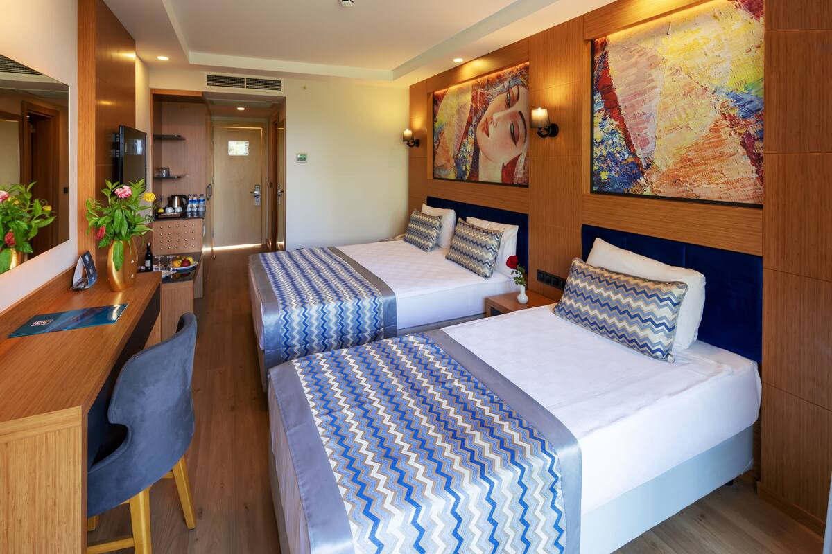 Een hotelkamer met twee bedden, een bureau met stoel, een spiegel en een schilderij aan de muur.