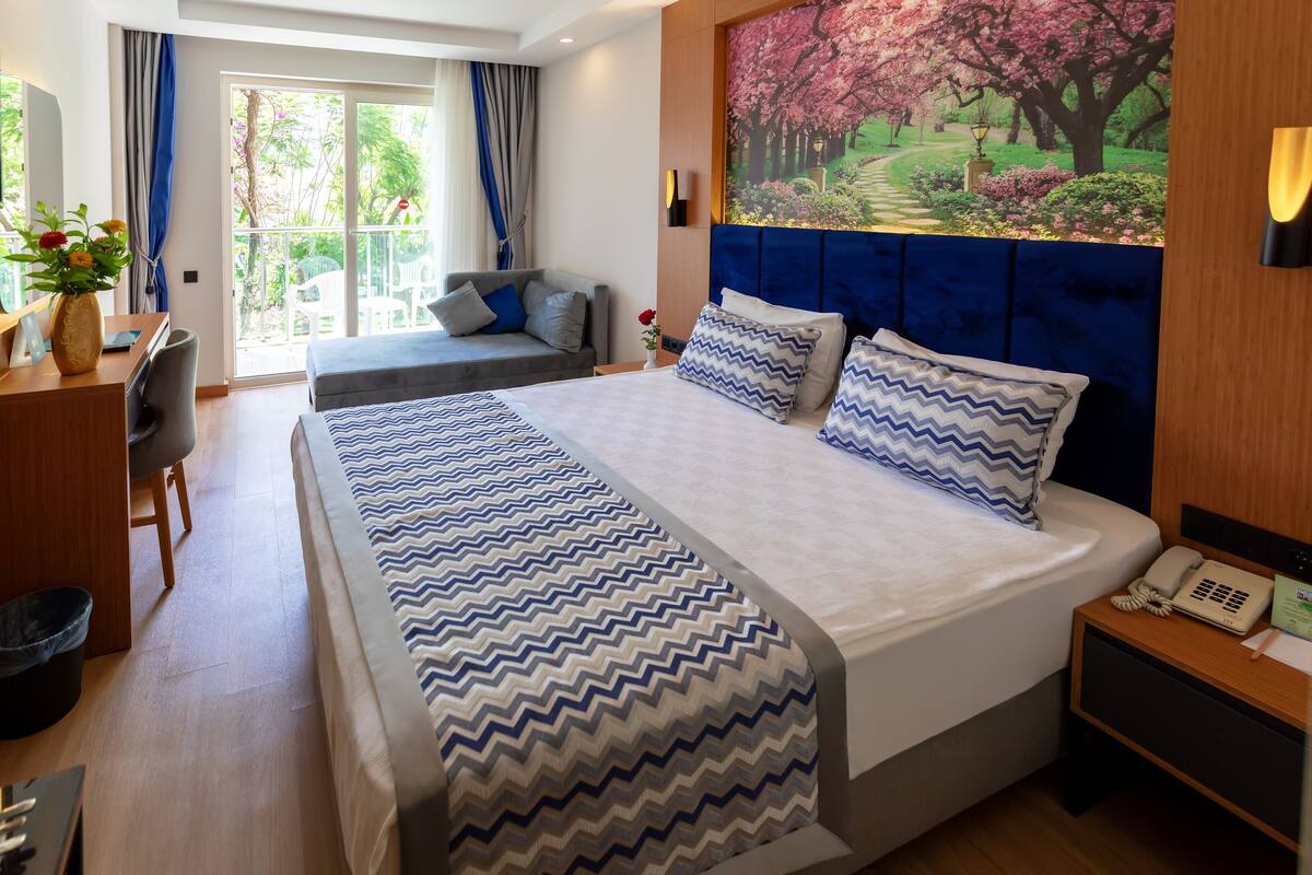 Een hotelkamer met een groot bed, een bureau, een stoel en uitzicht op een tuin door het raam.