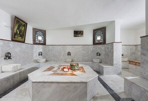 Un baño amplio con varios lavamanos, un lavabo central de mármol y detalles decorativos en las paredes.