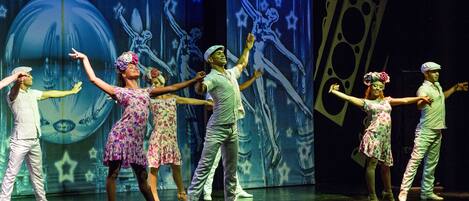 A stage with performers in various costumes, a large backdrop with stars and abstract shapes, and a dark floor.
