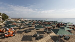 A beach with numerous sun umbrellas and lounge chairs, a wooden walkway, and a view of the sea.