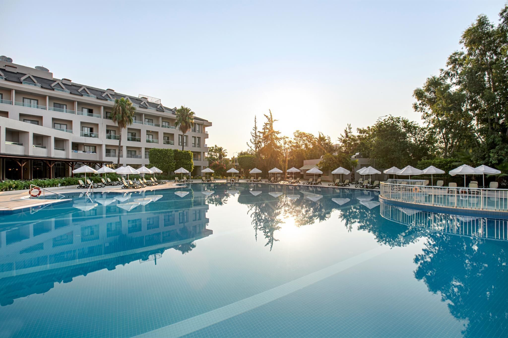 A swimming pool with lounge chairs and umbrellas, surrounded by a hotel building with balconies.