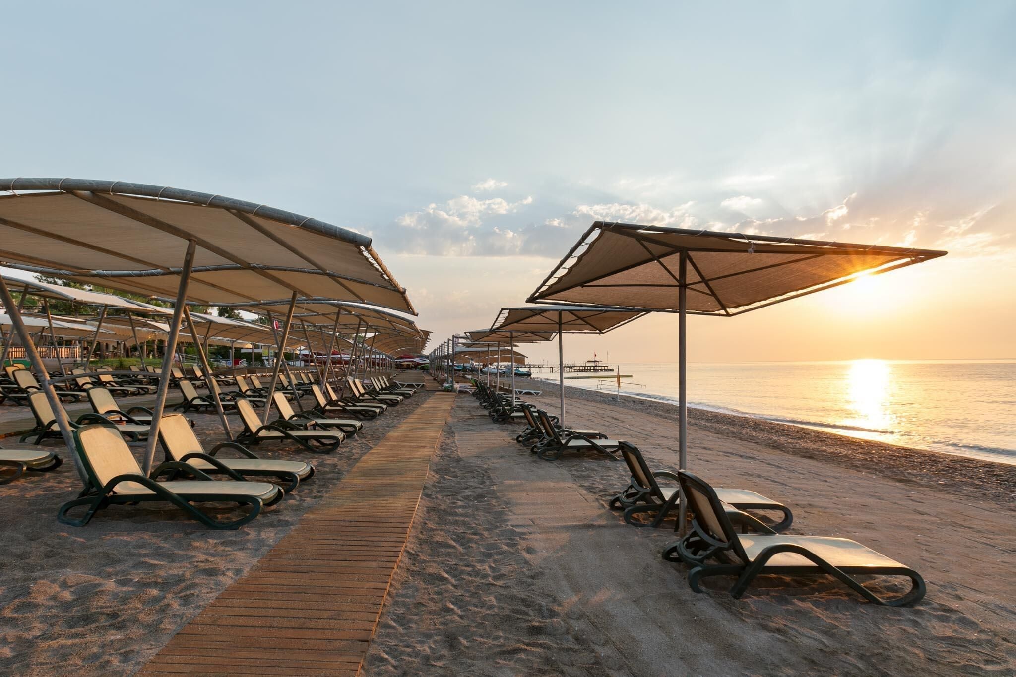 A beach with rows of sun loungers and umbrellas, a wooden walkway, and the ocean in the background.