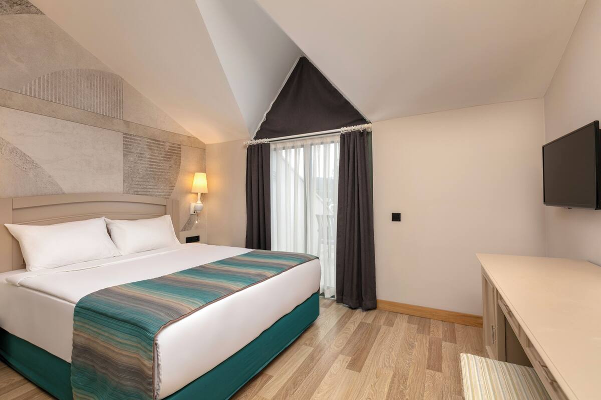 A hotel room with a bed, a desk, a TV, and a window with curtains.