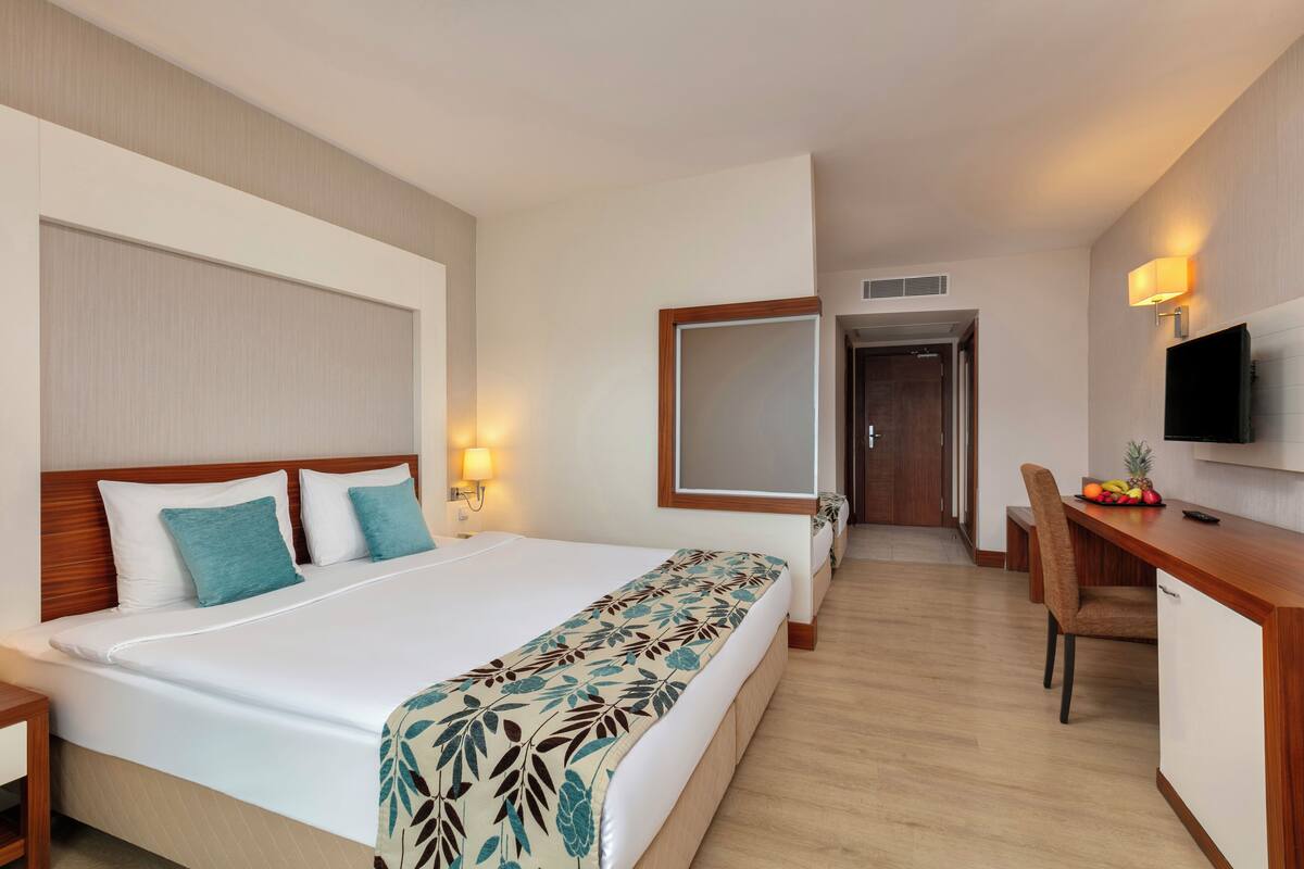 A hotel room with a large bed, a desk, a chair, a TV, and a fruit bowl.
