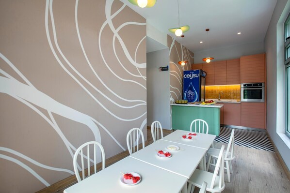 Un comedor moderno con sillas blancas y una mesa lista para una comida, una cocina con horno de acero inoxidable y una pared decorativa con motivos blancos.