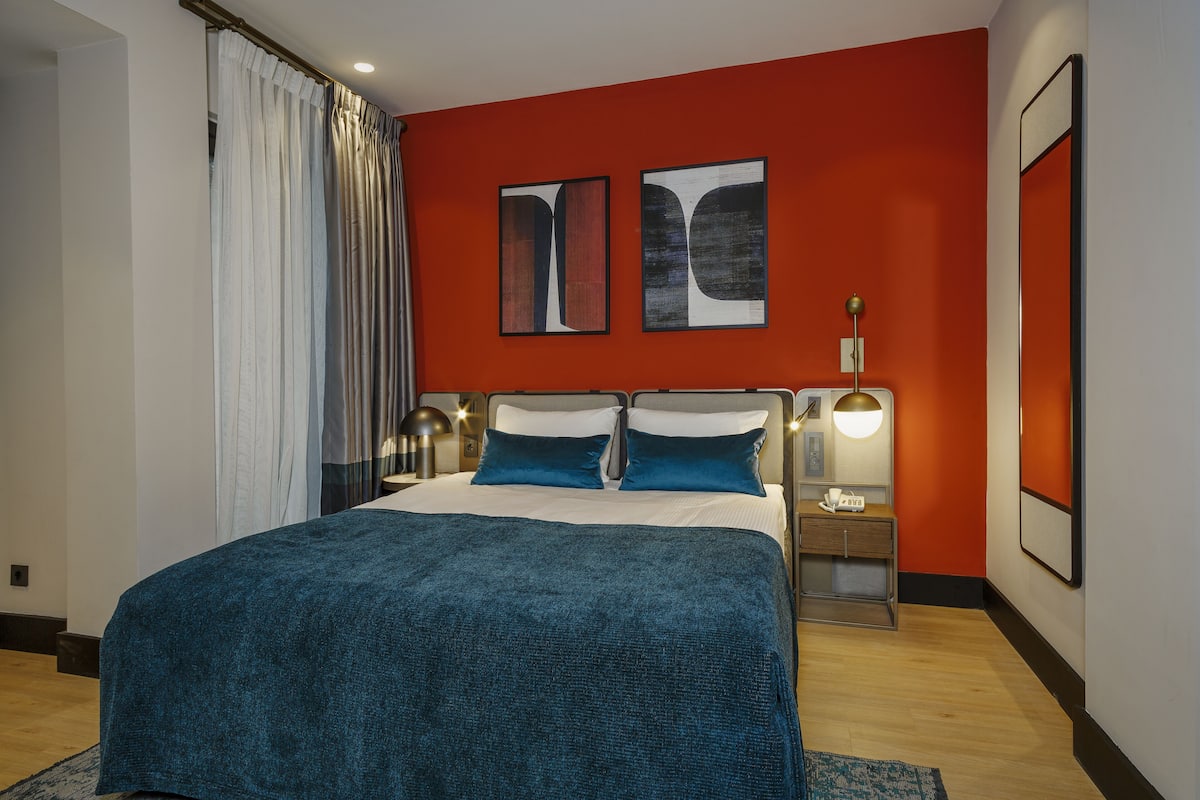 Quarto moderno com uma cama grande, duas mesas de cabeceira com abajures e duas pinturas abstratas na parede.