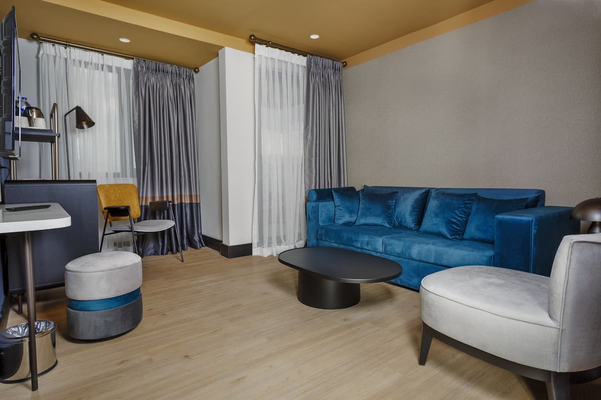 Uma sala de estar moderna com um sofá azul, uma poltrona cinza, uma mesa de centro redonda, uma mesinha redonda e uma televisão.
