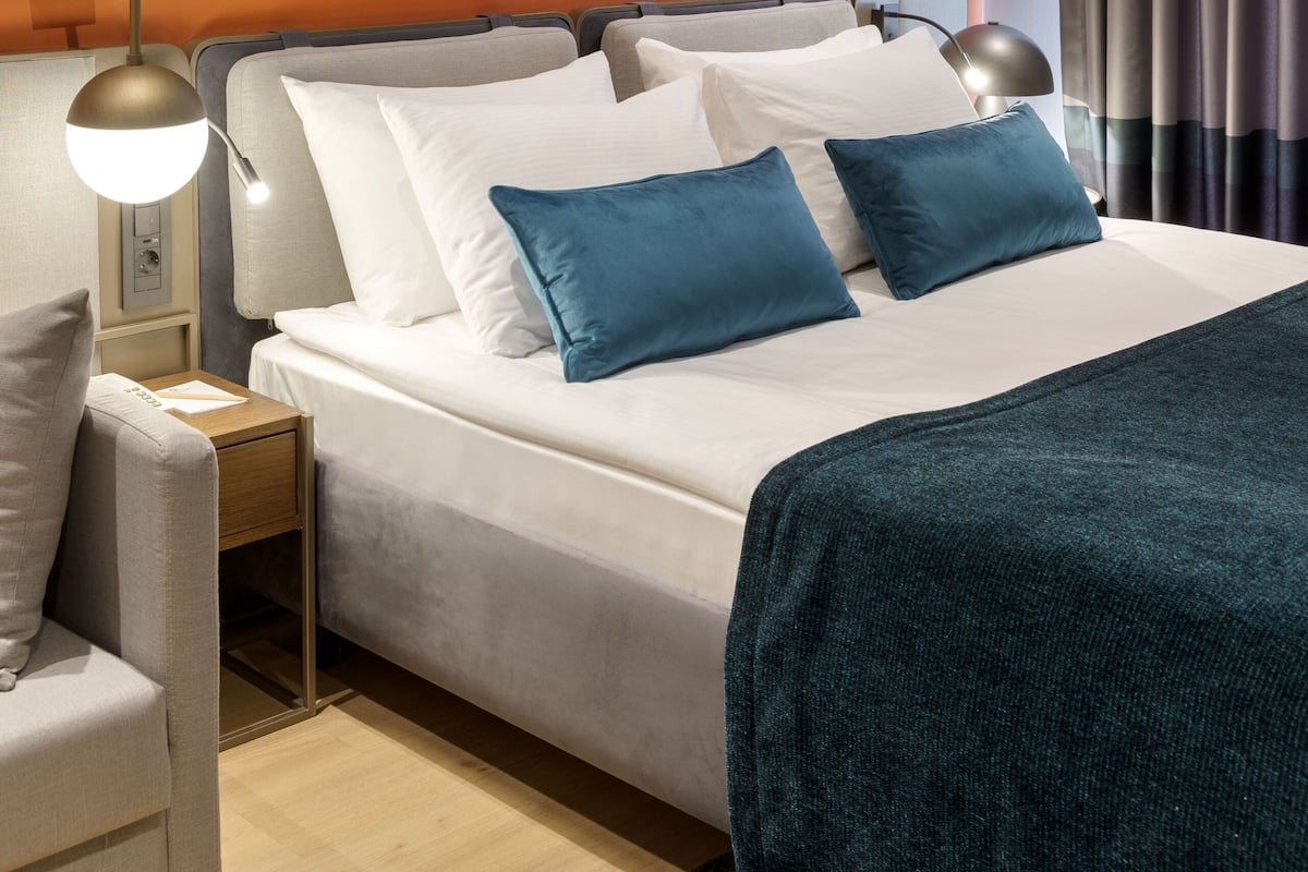 Quarto de hotel moderno com uma cama grande, mesa de cabeceira, luminária e obras de arte na parede.