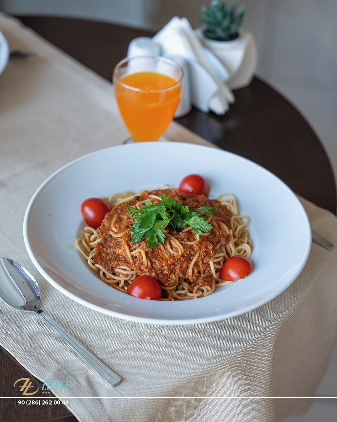 Un plato de espagueti con salsa de carne, adornado con perejil y tomates cherry, sobre un plato blanco.