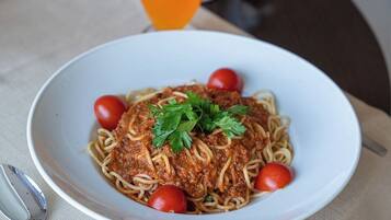 Un plato de espagueti con salsa de carne, adornado con perejil y tomates cherry, sobre un plato blanco.