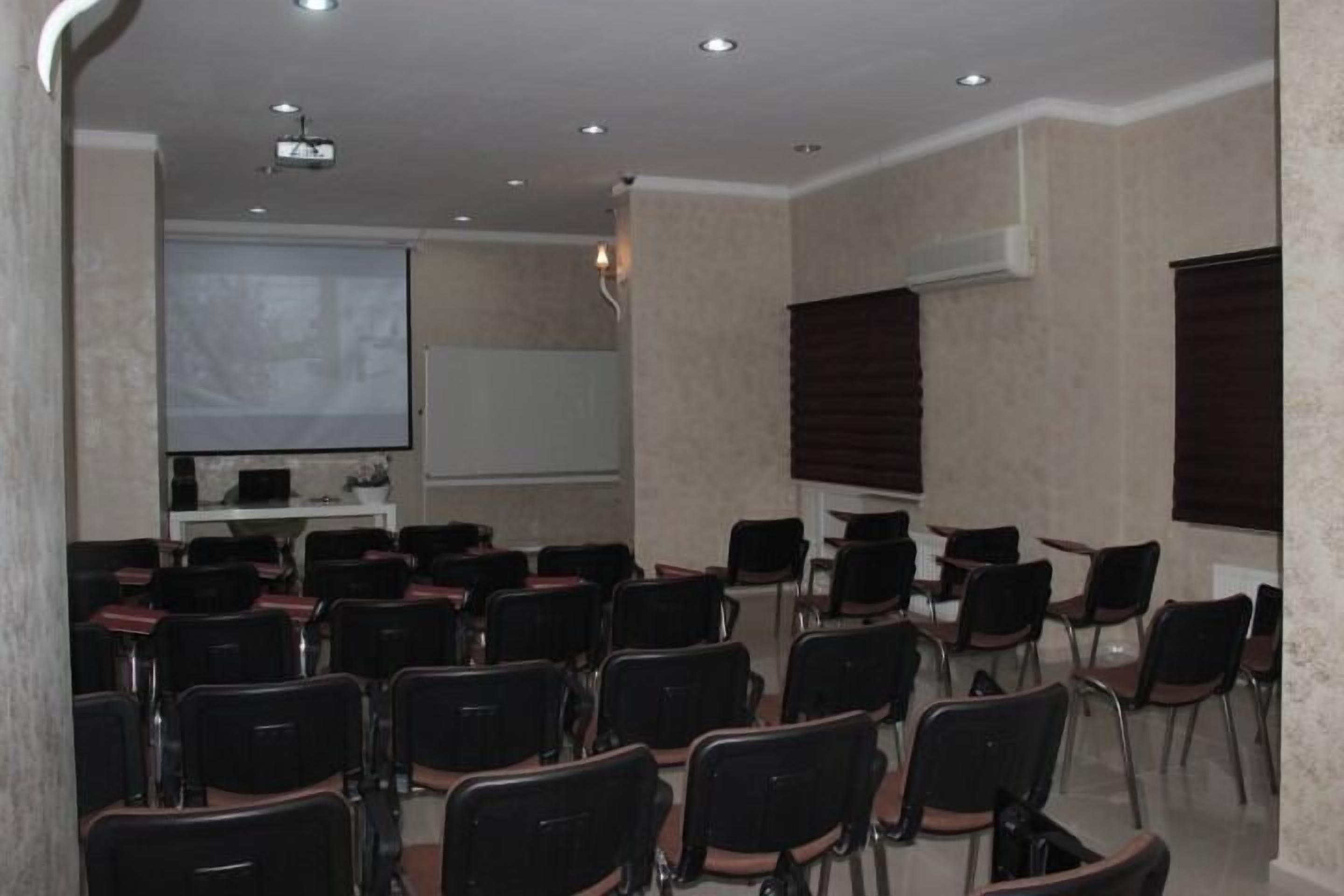 A conference room with rows of chairs, a projector screen, a whiteboard, and a presentation screen.