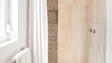 Une douche aux carreaux beiges, une porte en verre et un pommeau de douche en métal.