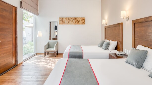 A hotel room with two beds, a wooden floor, a chair, a lamp, and a painting on the wall. - Quinta Allende (Querétaro)