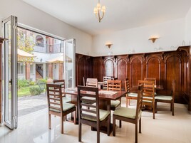 Un comedor con una gran mesa de madera y sillas, una araña y vistas a un patio a través de puertas de vidrio.