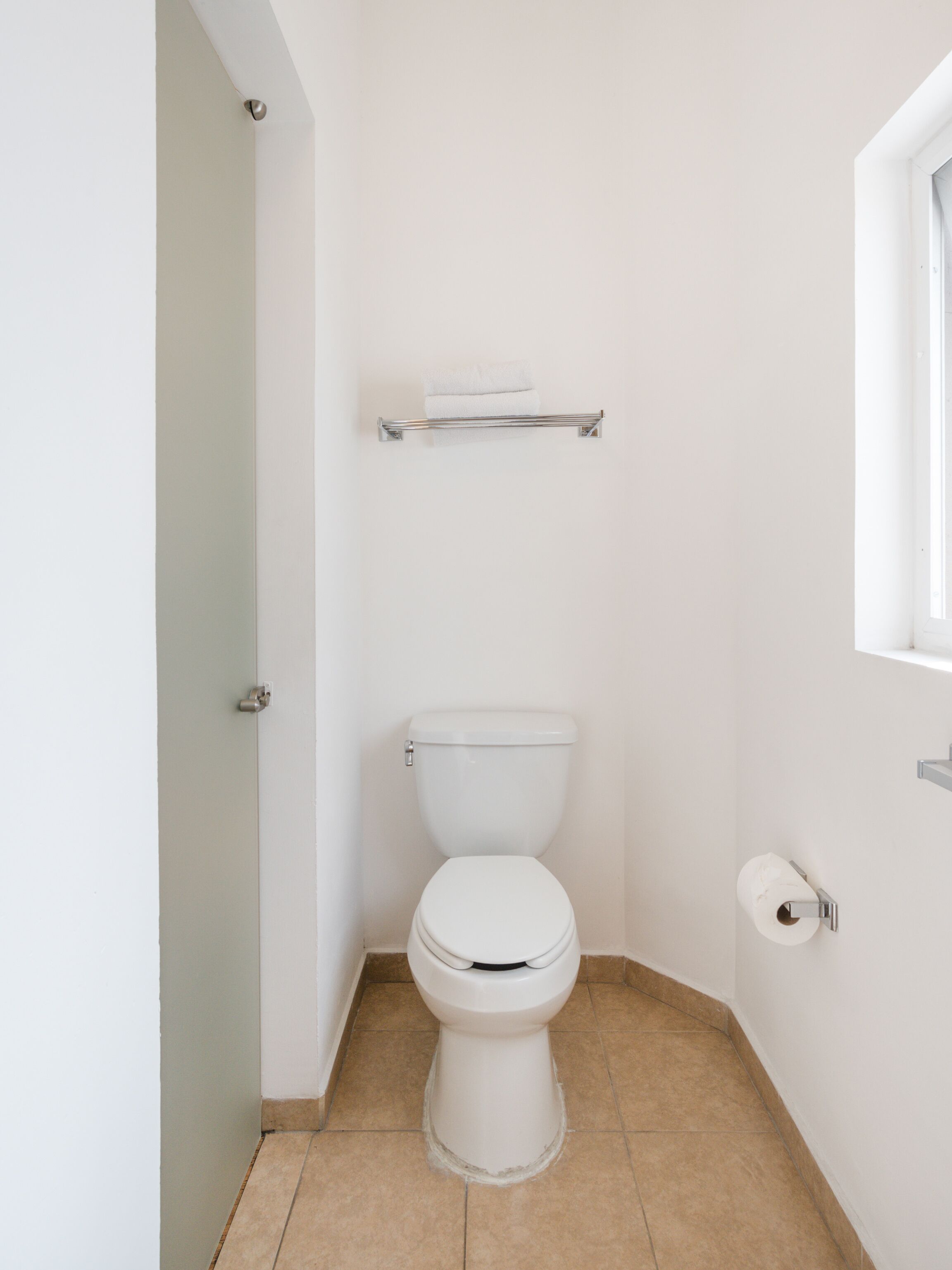Un baño pequeño y limpio, con inodoro blanco, un perchero encima y un dispensador de papel higiénico a la derecha.