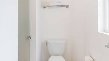 Un baño pequeño y limpio, con inodoro blanco, un perchero encima y un dispensador de papel higiénico a la derecha.