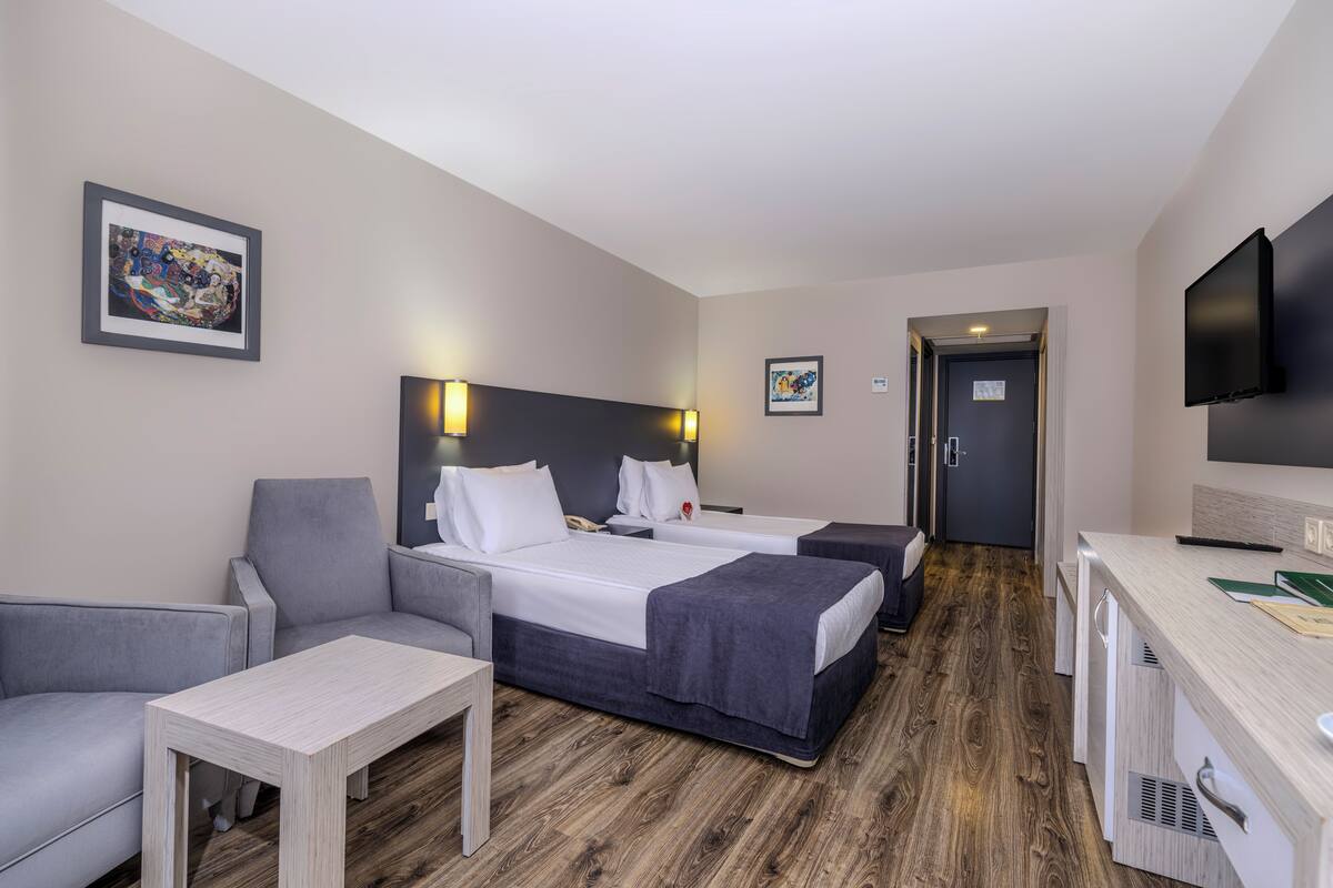 A hotel room with two beds, a desk, a chair, a TV, and artwork on the walls.