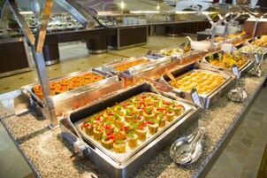 Buffet com diversas opções de comida, incluindo petiscos e saladas, dispostos em um balcão com utensílios de servir.
