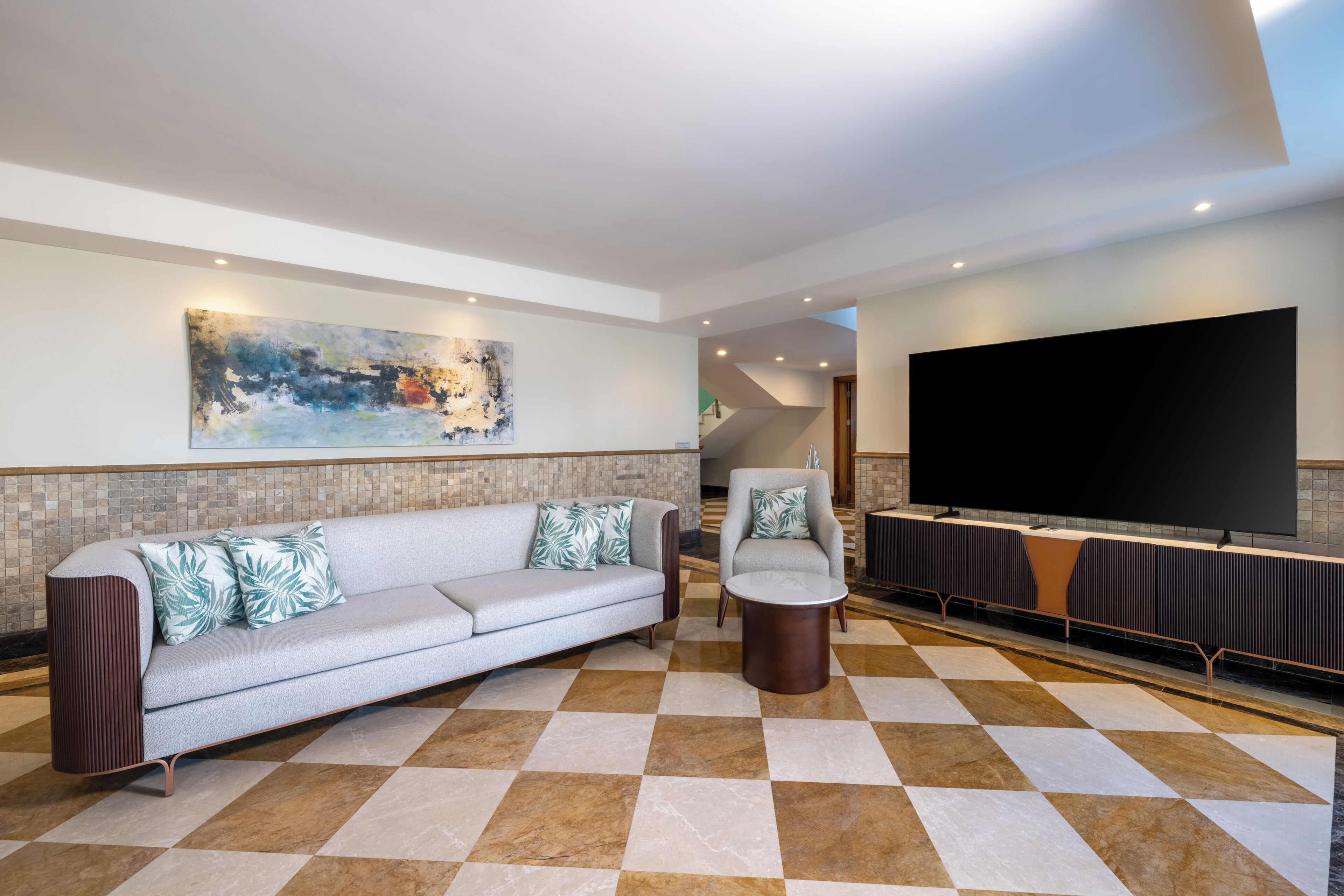A modern living room with a sofa, armchair, and a large flat-screen TV.
