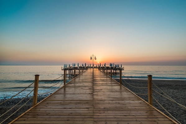 A wooden pier leading to a beach with a sunset in the background. - Nirvana Mediterranean Excellence - All Inclusive  (Kemer)