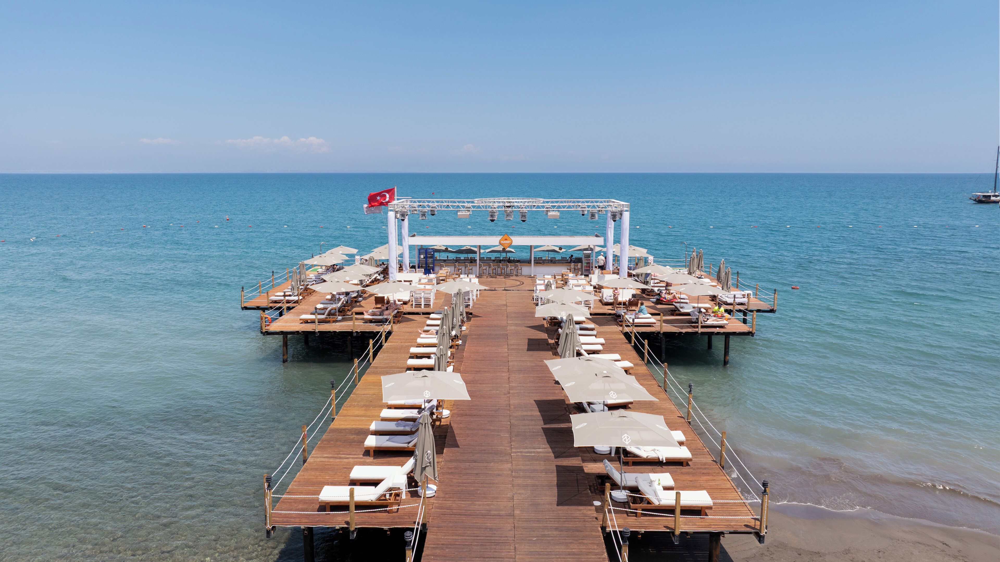 A pier with sun loungers and umbrellas, a flag, and a view of the sea.