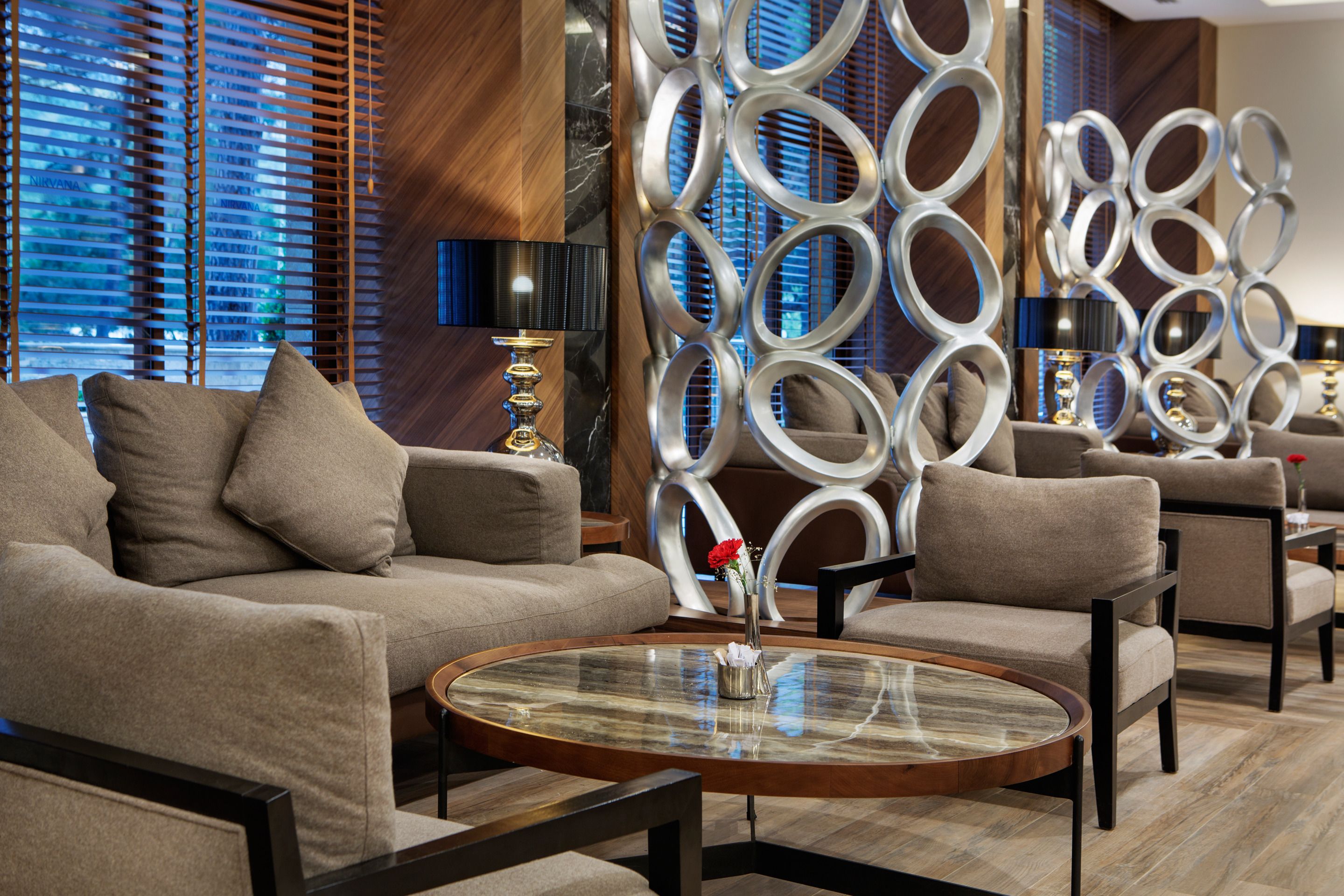 A modern living room with a round glass coffee table, beige sofas, and a decorative wall with circular patterns.