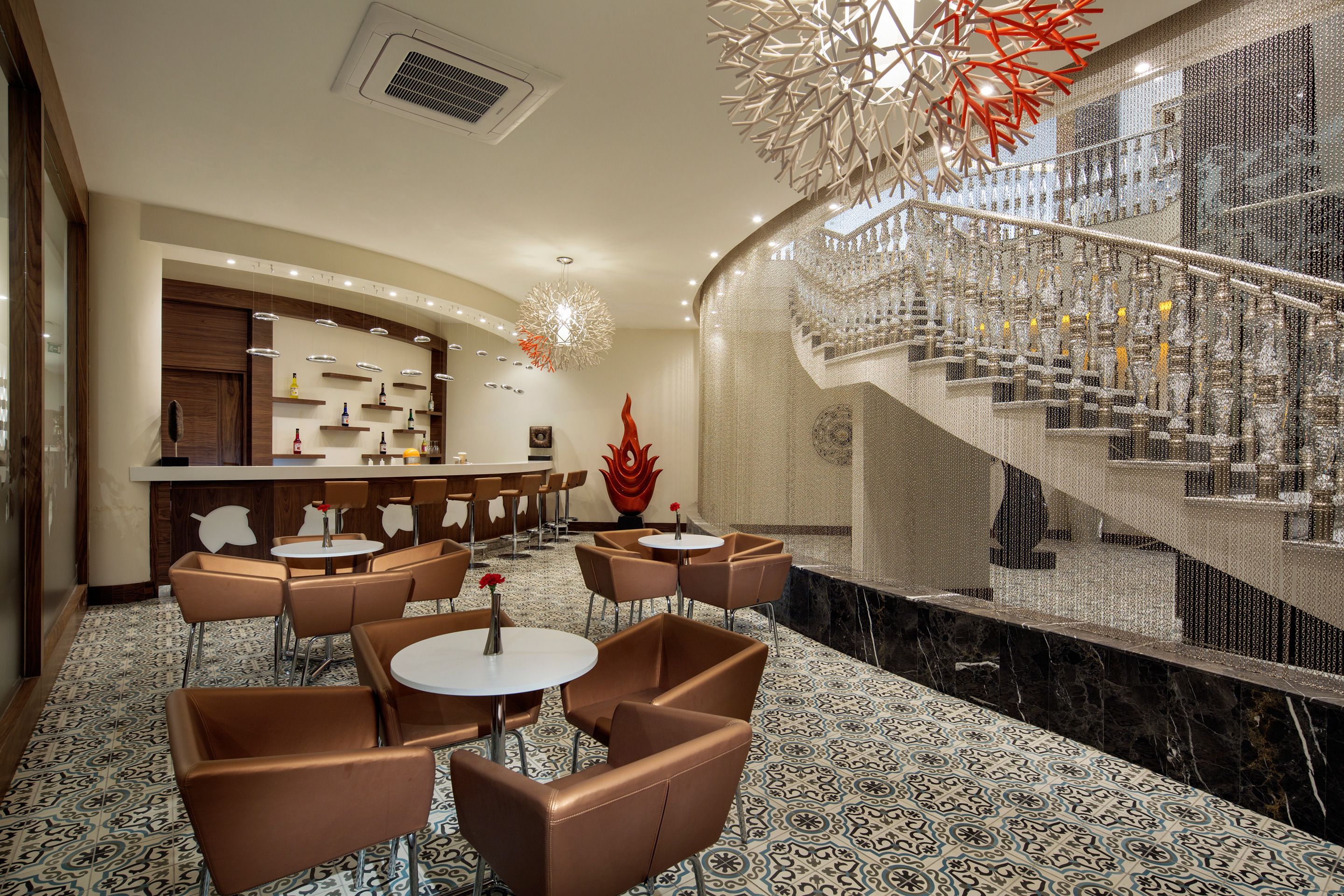 A hotel lobby with a bar area, seating arrangements, and a staircase with a decorative railing.