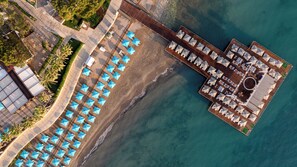 Luchtbeeld van een resort met een strand, een houten pier en een zwembad.