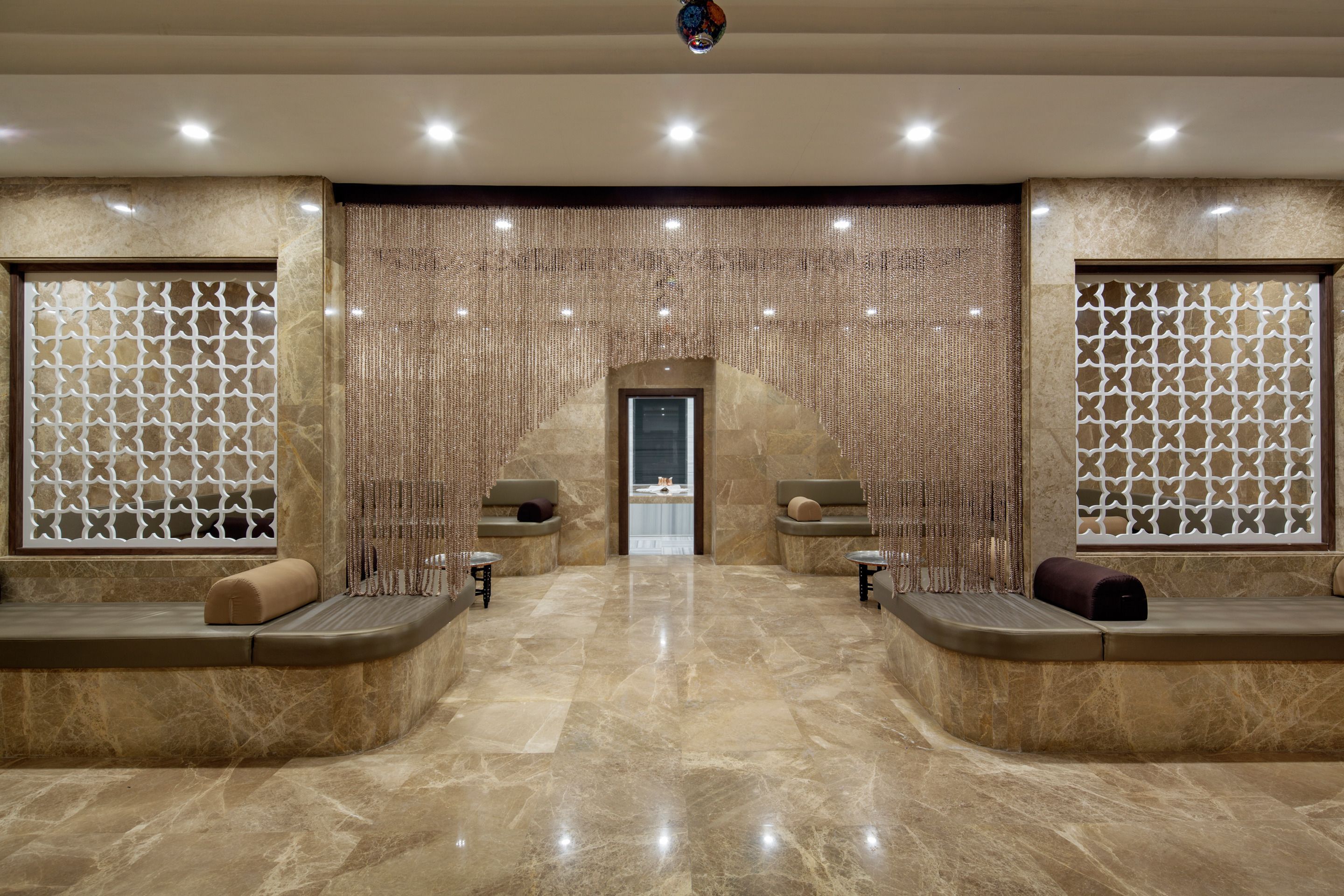 A spa area with a marble floor, two seating areas with cushions, and a decorative wall with a geometric pattern.