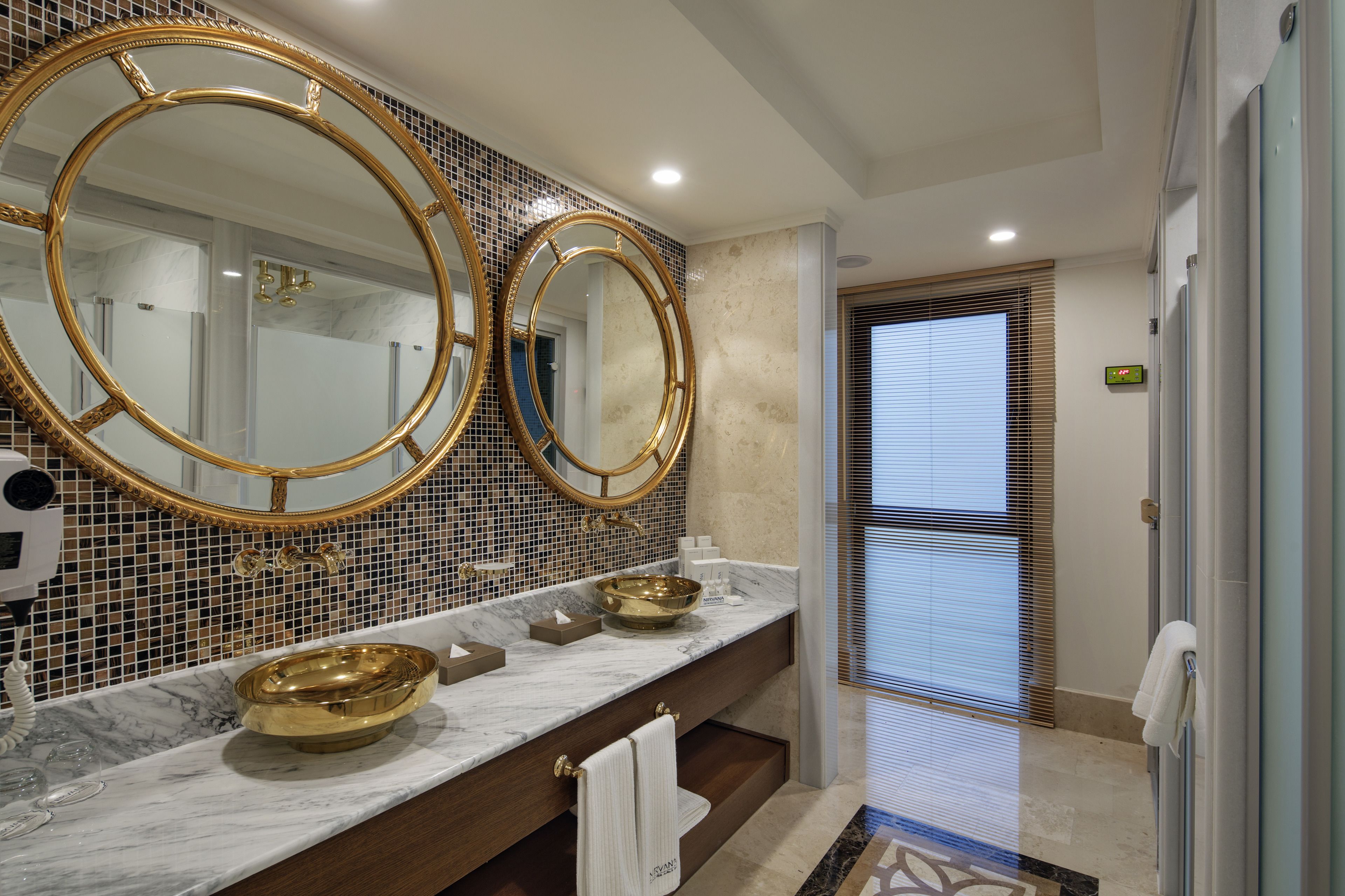 A bathroom with two large gold-framed mirrors, a marble countertop, and a gold bowl sink.