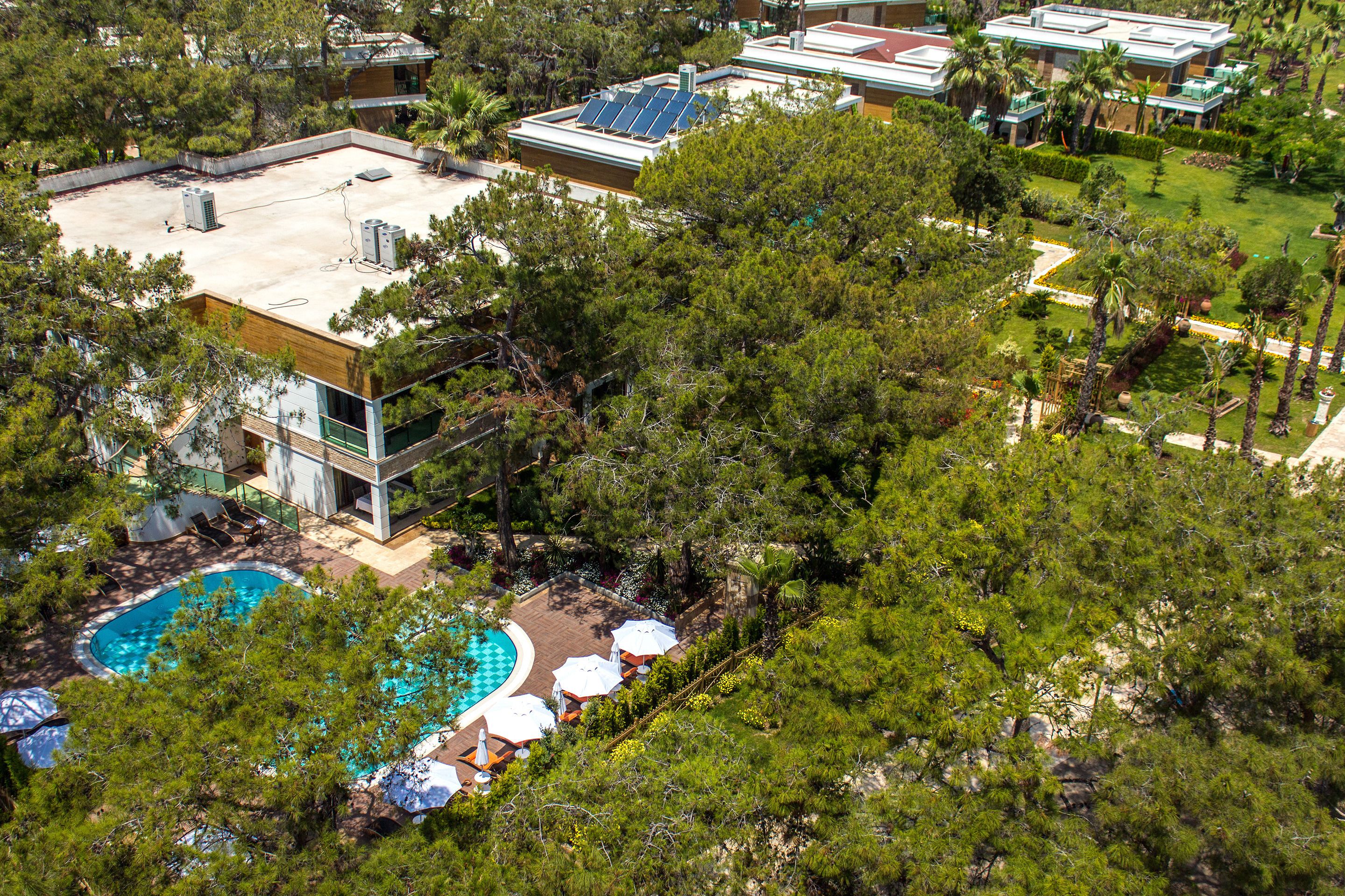 An aerial view of a resort with a swimming pool, sun loungers, and a rooftop with solar panels.
