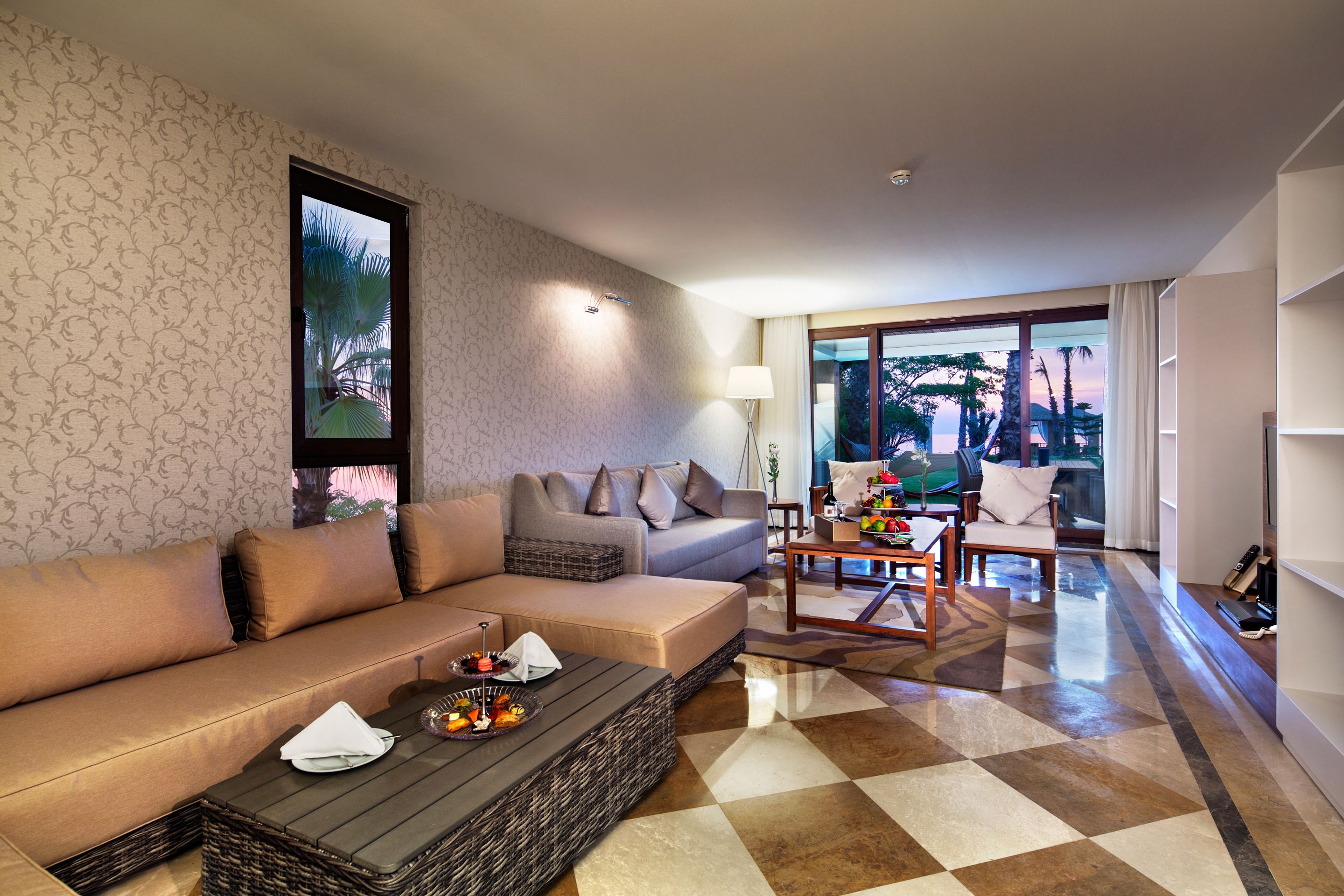 Una sala de estar moderna con un sofá, una mesa de centro y vistas a palmeras a través de una ventana.