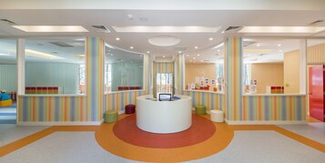 Un área de recepción de colores vivos, con un mostrador central, paredes a rayas y zonas de estar coloridas.
