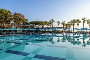 Una piscina con sillas de descanso y sombrillas, rodeada de palmeras y un edificio con un letrero.
