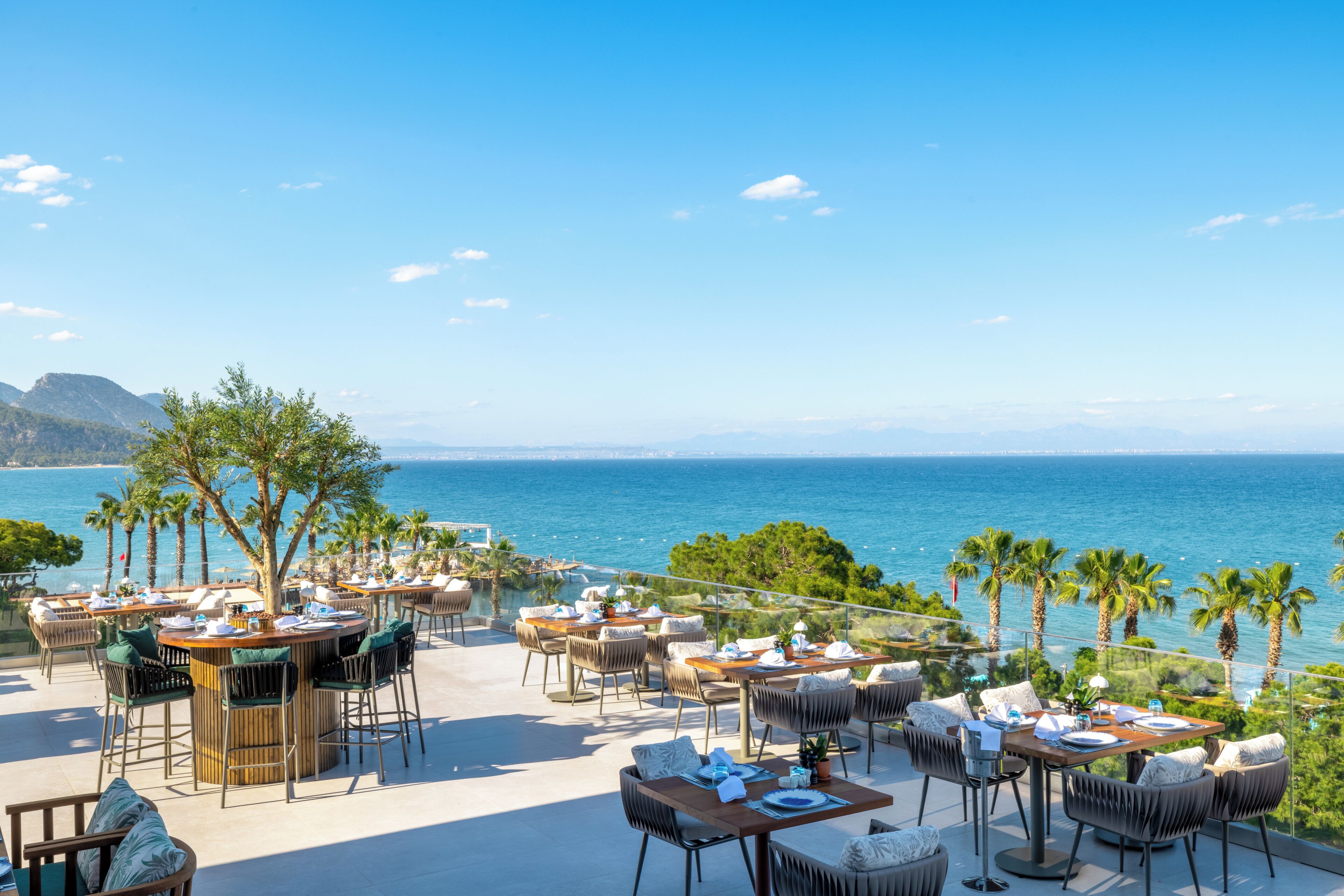 An outdoor dining area with tables and chairs, overlooking a body of water and a distant coastline.