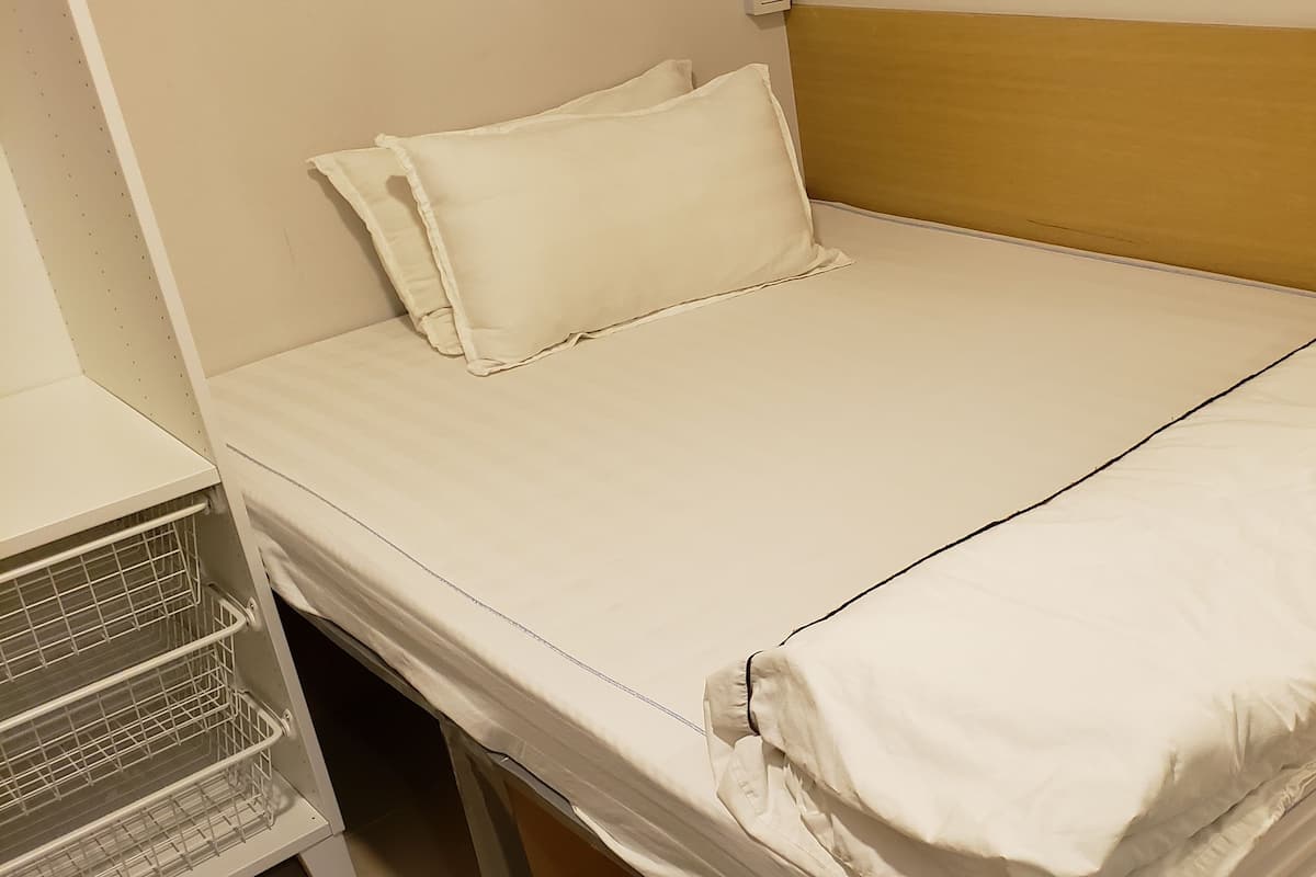 A single bed with a wooden headboard, a white mattress, and a white pillow.