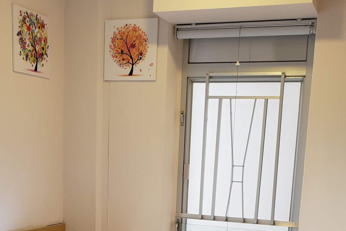 A single-bed room with a window, a bed with white bedding, and two wall-mounted paintings.