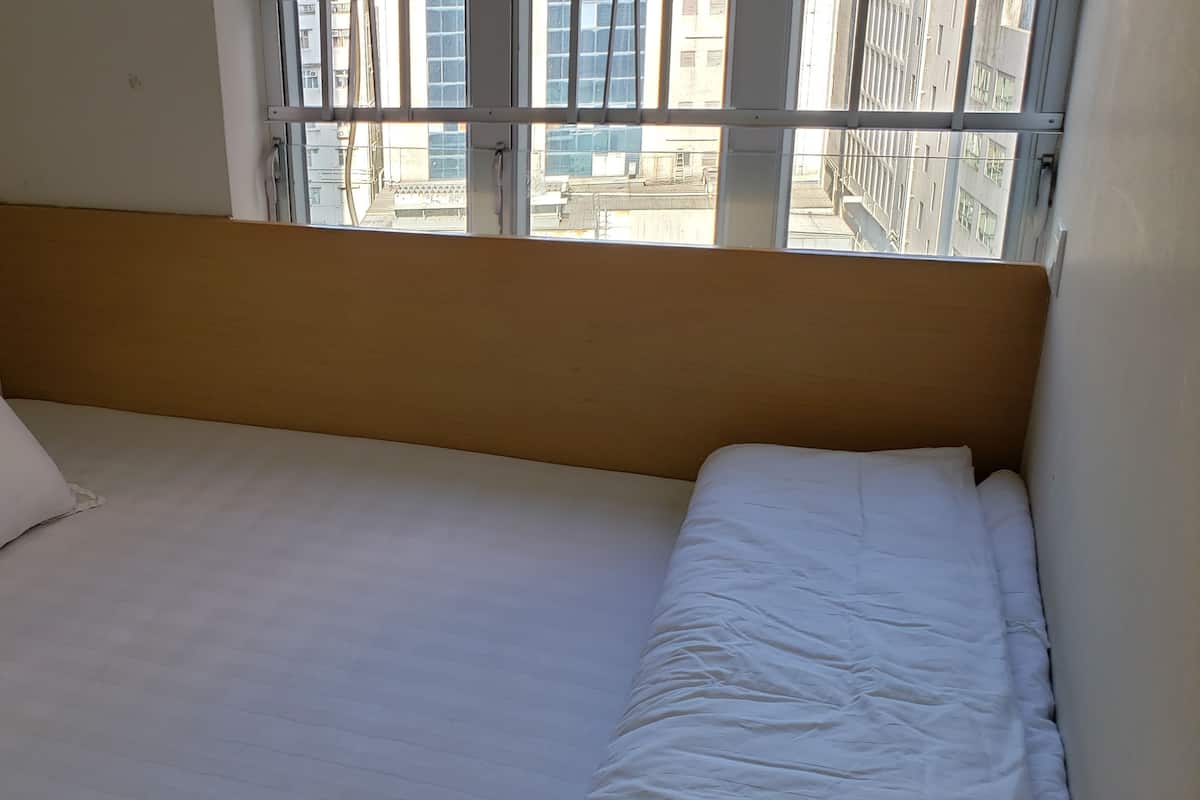 A single bed with white bedding and a wooden headboard in a room with a window.