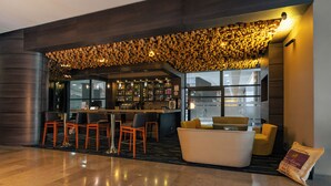 Un bar moderno con techo de madera original, taburetes y una zona de estar con sofá blanco y sillas amarillas.