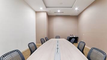 Una sala de conferencias con una larga mesa, seis sillas y una mesa pequeña con un ordenador portátil y una taza.