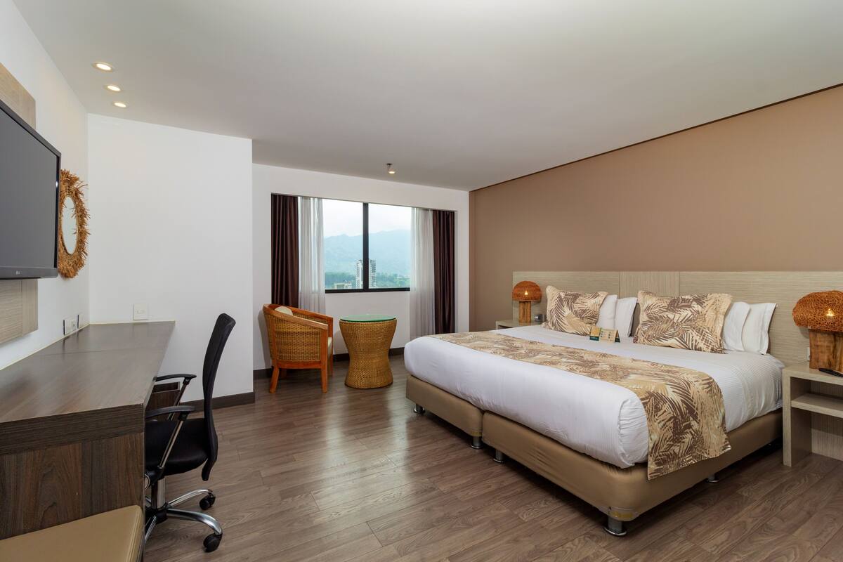 Una habitación de hotel con una cama grande, un escritorio, una silla, una mesita y un televisor.