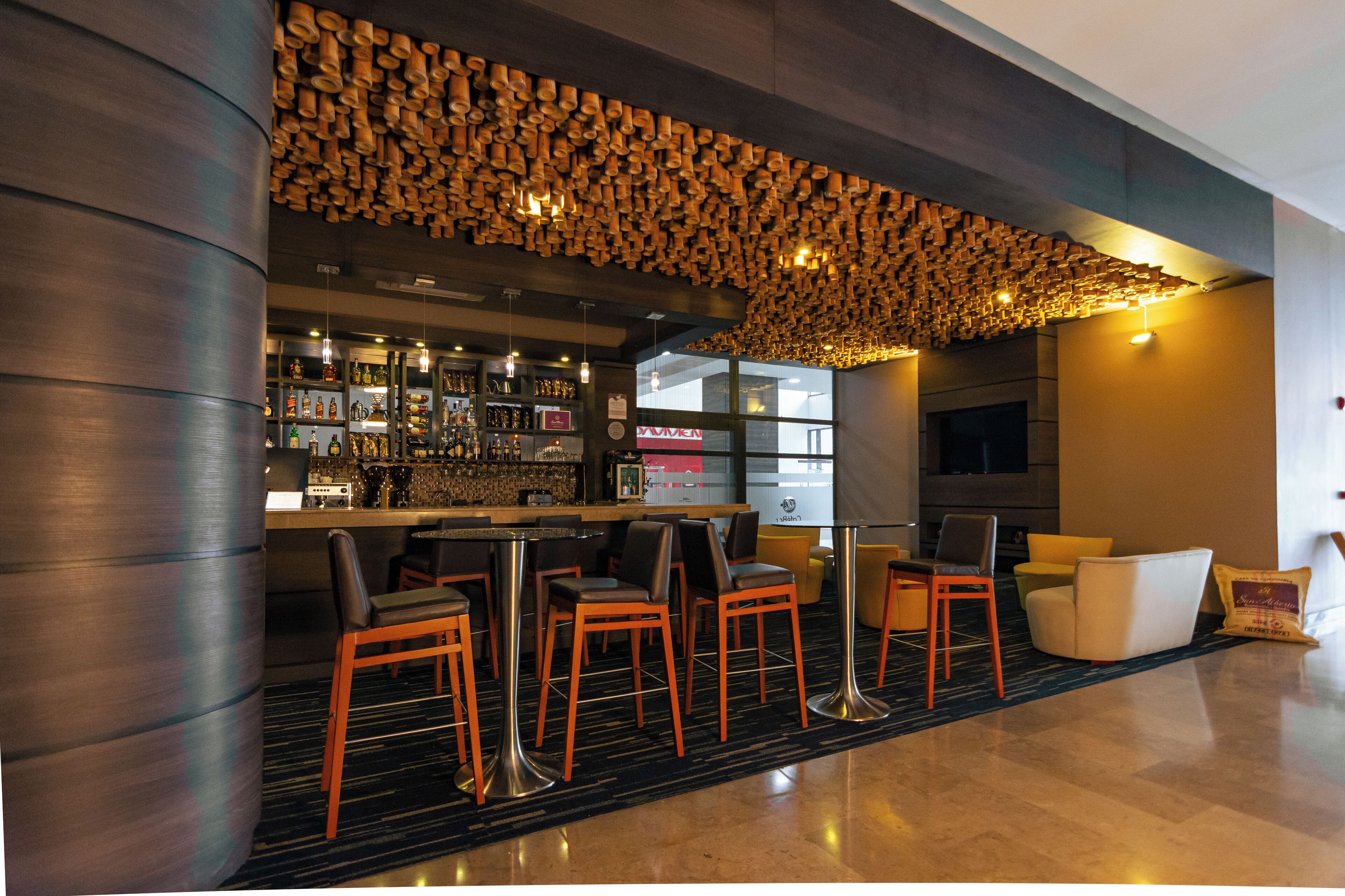 A modern bar area with a unique wooden ceiling, bar stools, and a seating area with a sofa and chairs.