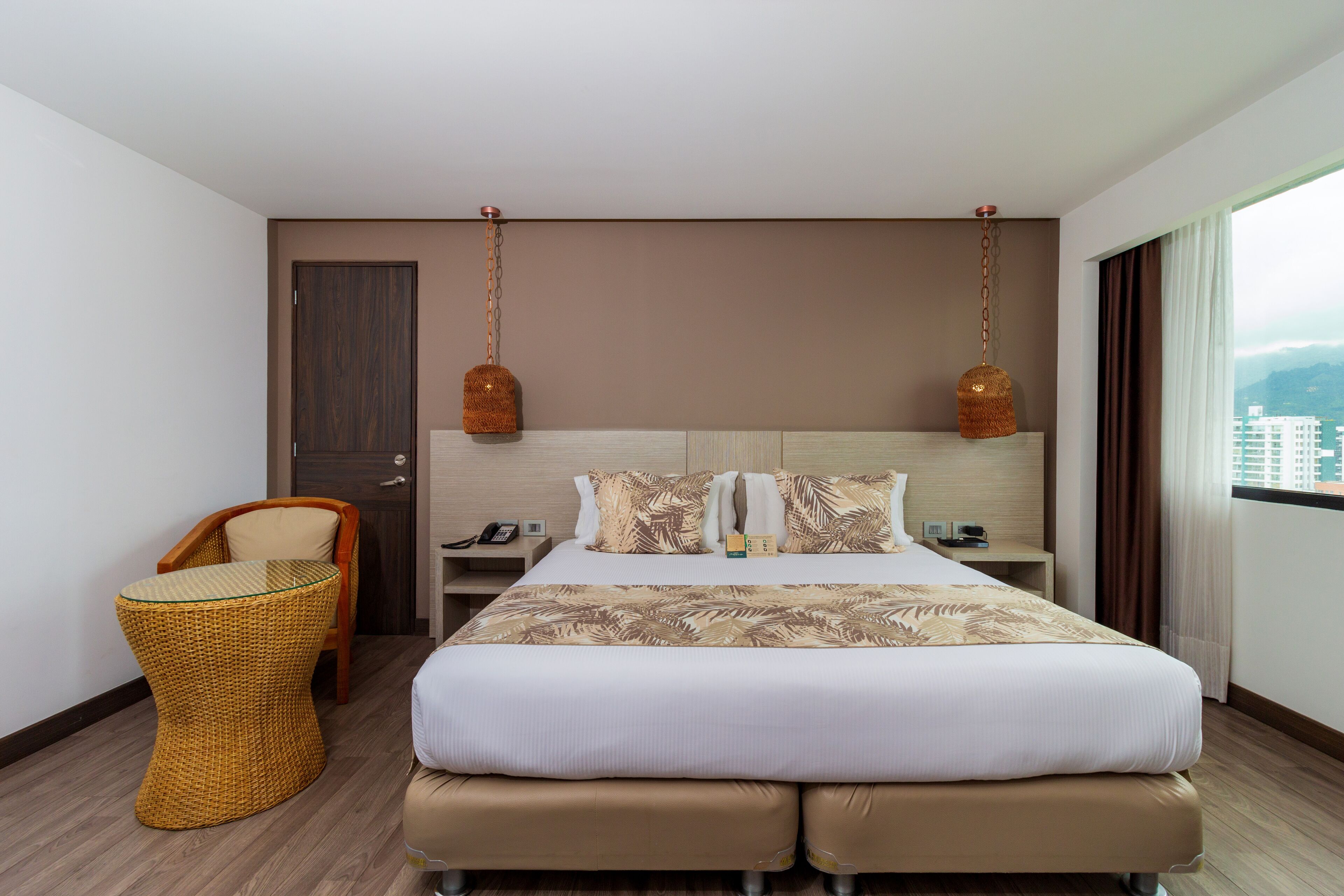Una habitación de hotel con una cama grande, una silla, una mesita de noche y una lámpara colgante.