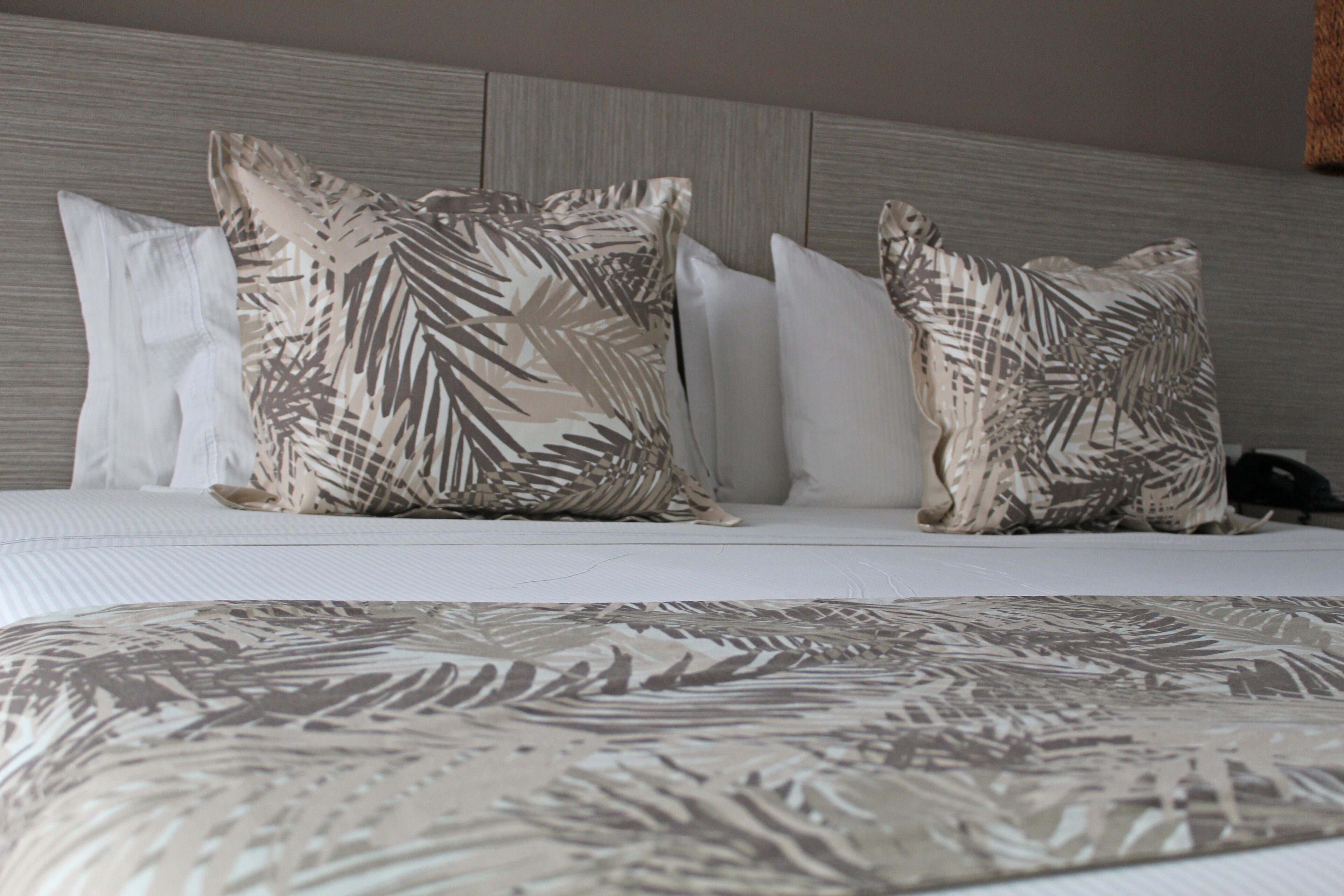 A bed with a patterned bedspread and multiple pillows, including a large one with a leaf design.