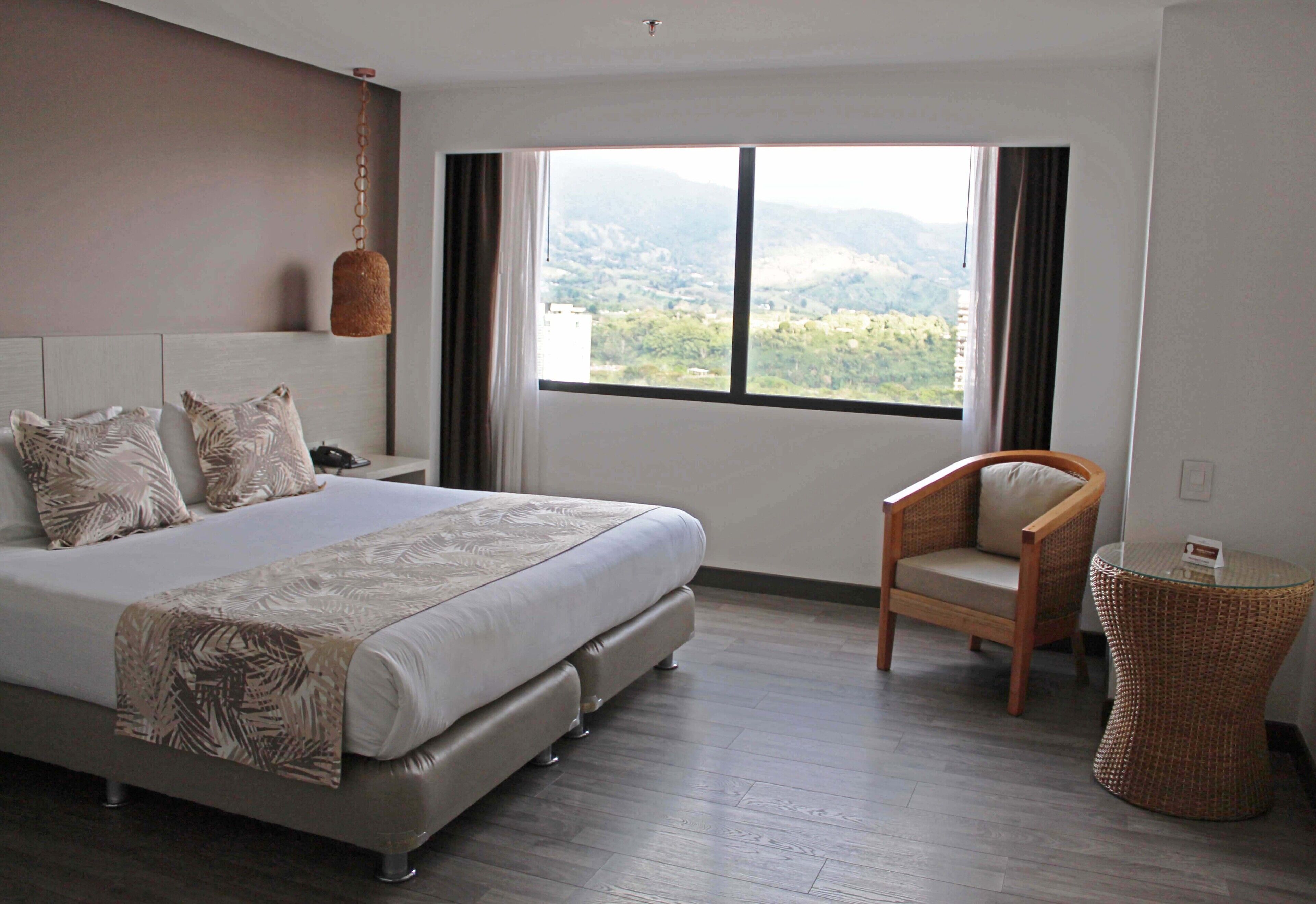 A bedroom with a large bed, a chair, a small table, and a view of mountains through a window.