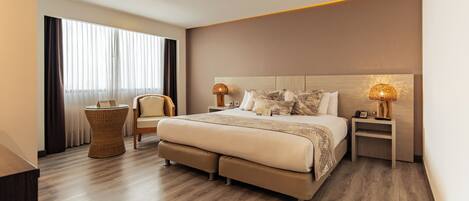A modern hotel room with a large bed, two bedside tables, a chair, and a large window with curtains.