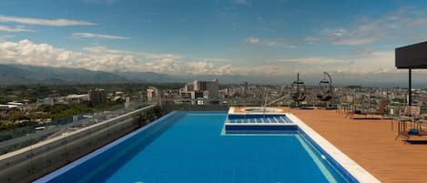 A rooftop pool with a city view, surrounded by lounge chairs and a wooden deck.