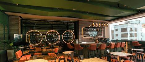 A modern restaurant interior with round tables, bar seating, and a view of the city through large windows.