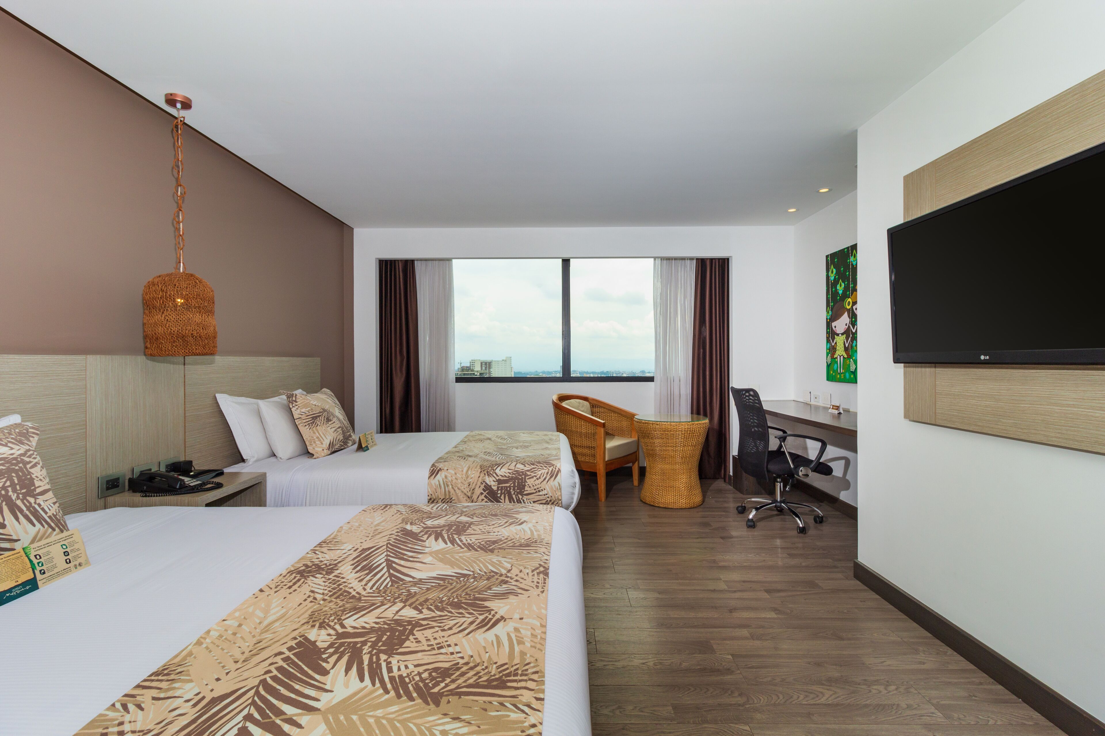 A hotel room with two beds, a desk, a chair, a television, and a large window.